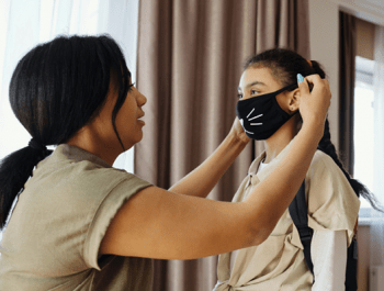 A mother putting a mask on her daughter.