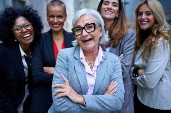 Portrait of smiling entrepreneurs in suits from an empowered happy women business in city. A group of five joyful female of diverse races and ages looking laughing at camera with arms crossed outdoor